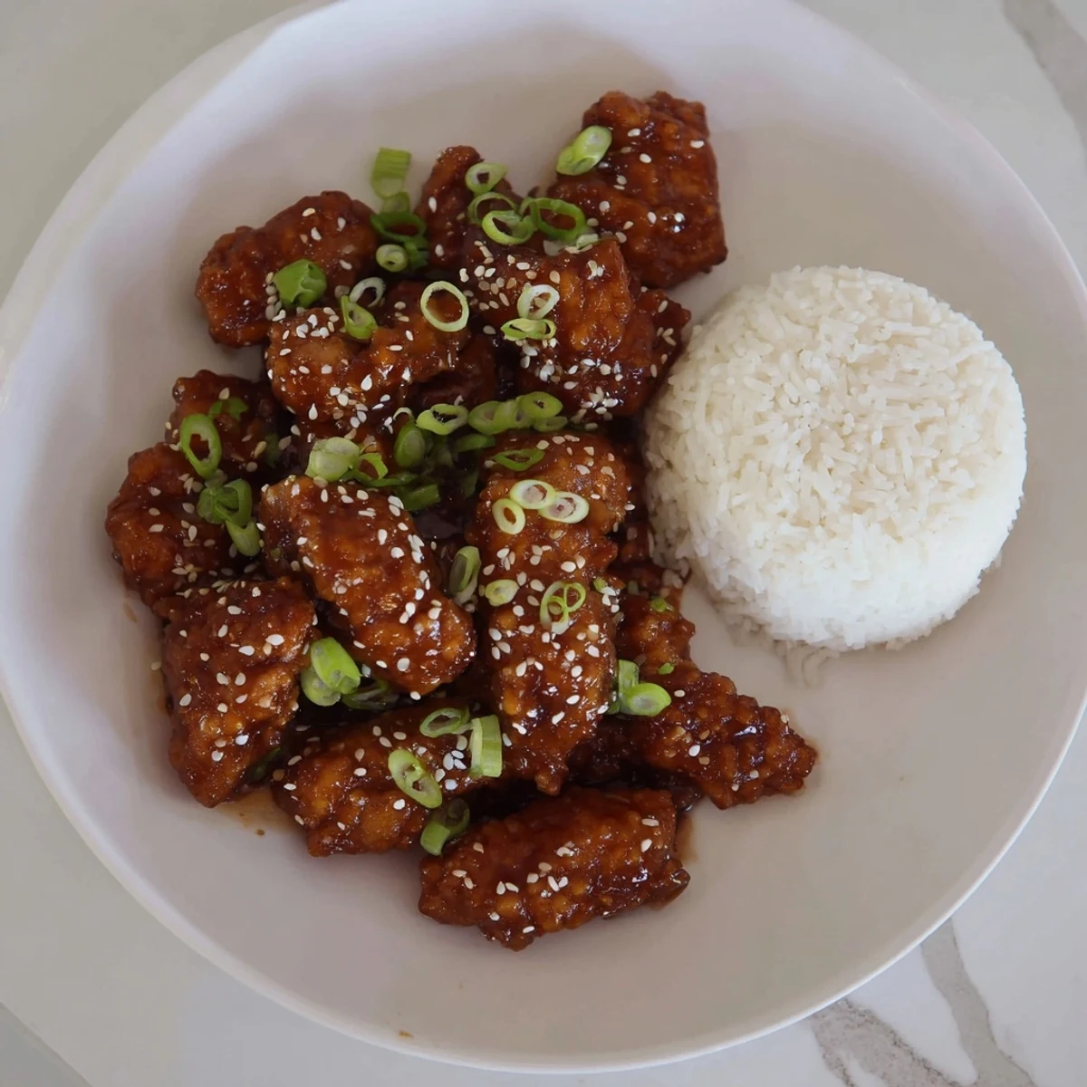 Golden Mongolian chicken pieces coated in a rich brown glaze with sesame seeds