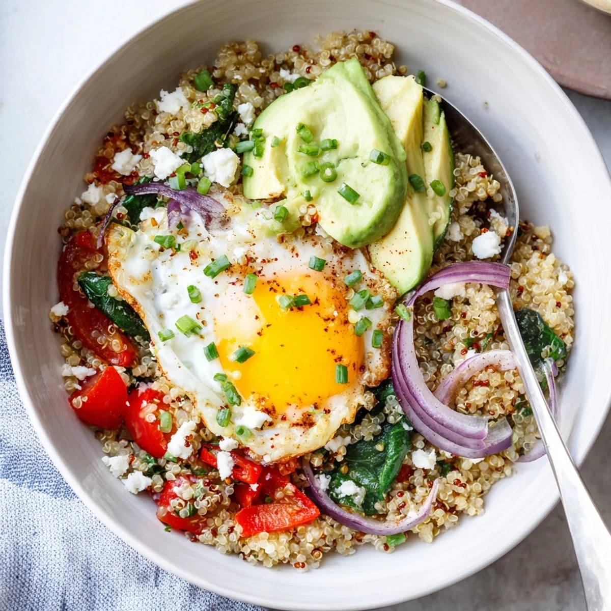 Golden fried egg resting atop fluffy savory quinoa breakfast bowl with colorful sautéed vegetables