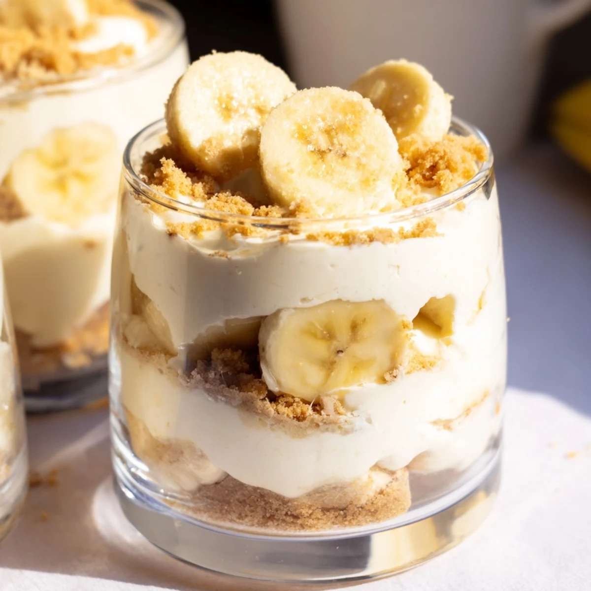 Individual no bake banana pudding cheesecake cups topped with golden cookie crumbs and sliced bananas