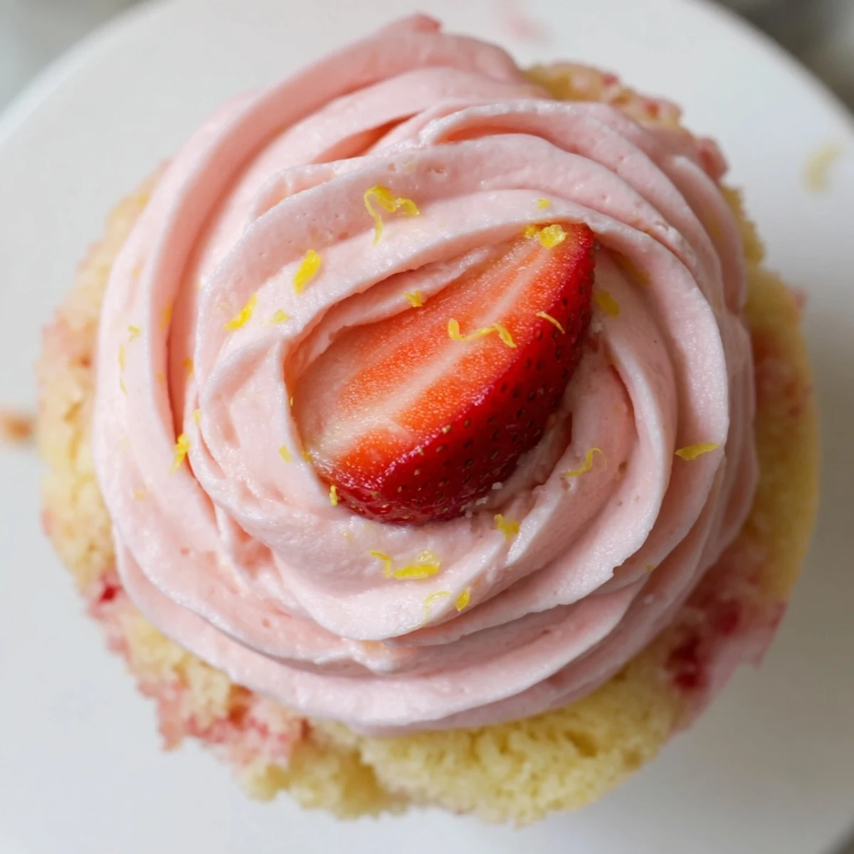 Pink strawberry lemonade cupcakes topped with swirled buttercream frosting on a rustic white cake stand