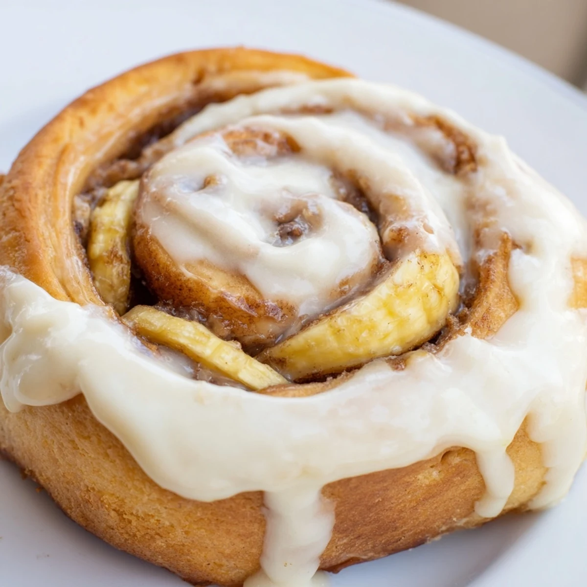 Golden banana cinnamon rolls topped with creamy white glaze on a rustic wooden board