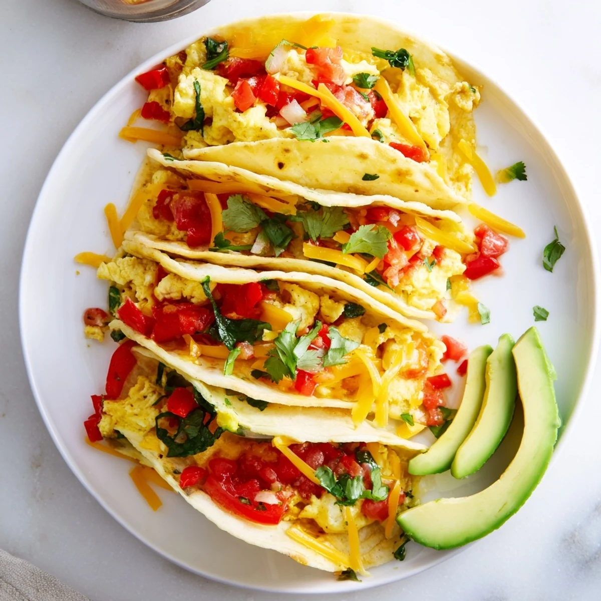 Crispy oven-baked breakfast tacos topped with fresh avocado, salsa, and cilantro garnish
