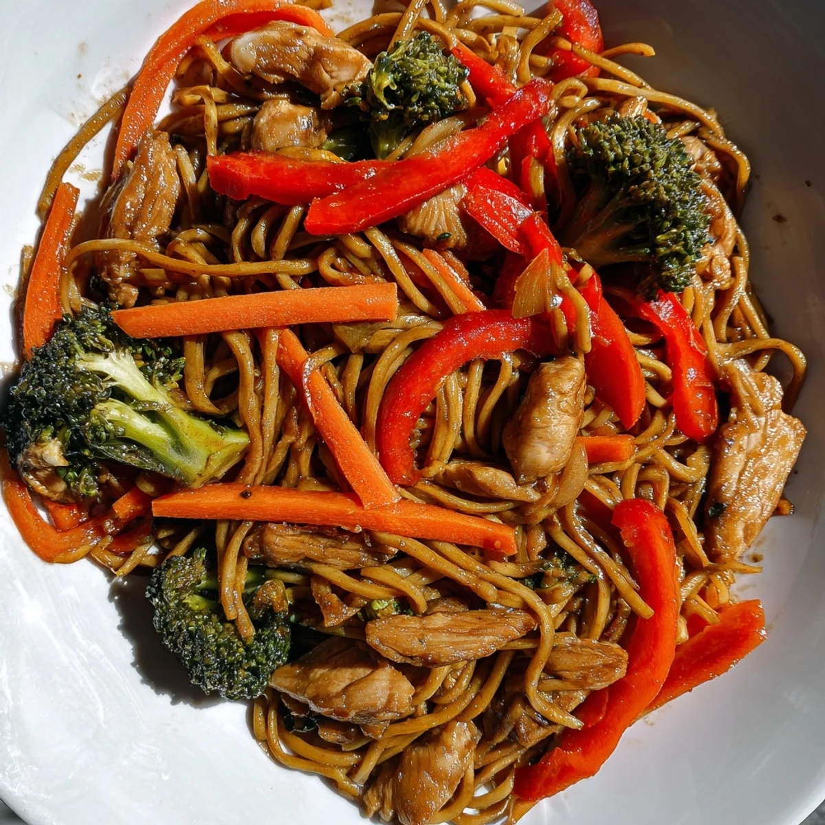 Steaming plate of savory garlic chicken lo mein featuring tender meat and crisp broccoli florets