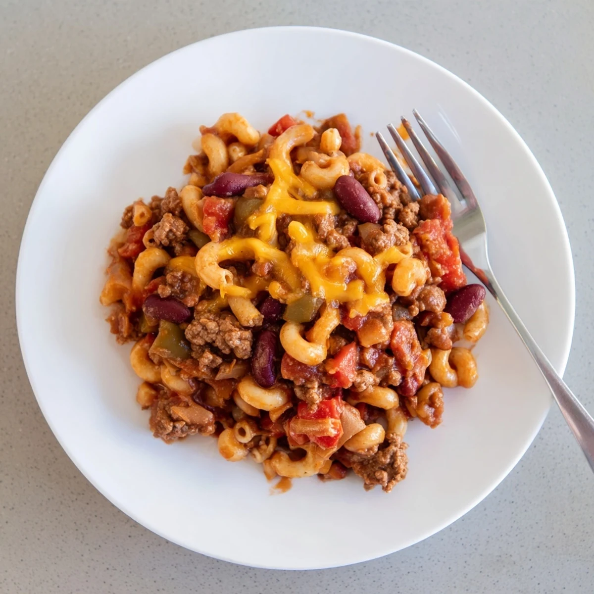 Spoon lifted from steaming chili mac and cheese recipe showcasing kidney beans and ground beef