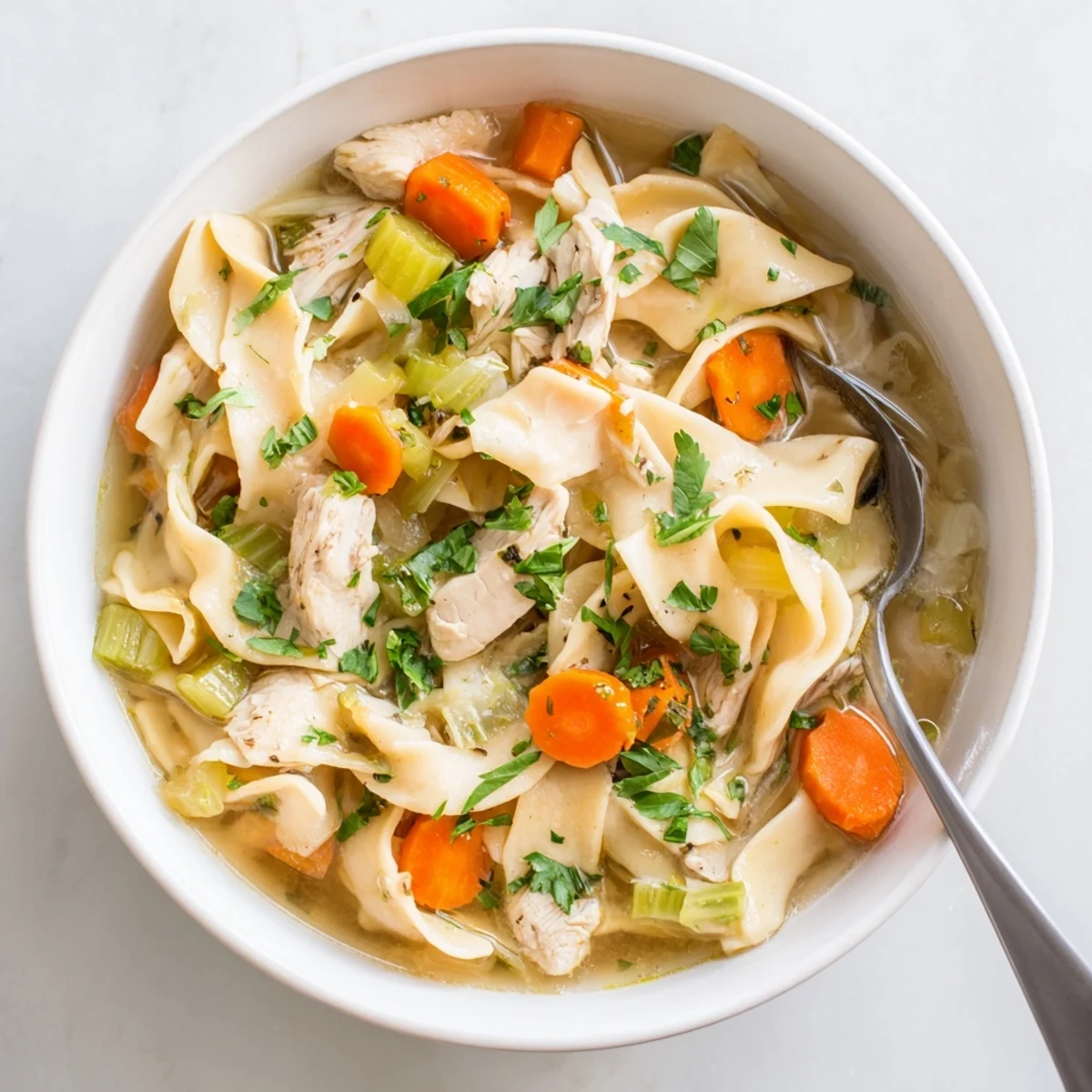 Creamy one pot chicken and noodles featuring egg noodles, sliced carrots, and celery in a rich chicken broth