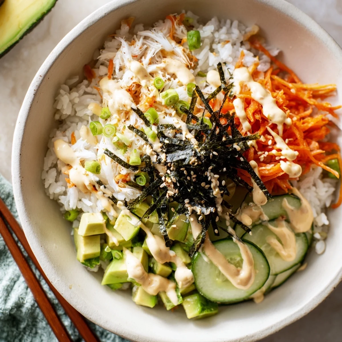 Deconstructed California roll sushi bowl drizzled with spicy mayo and sesame seeds over seasoned rice