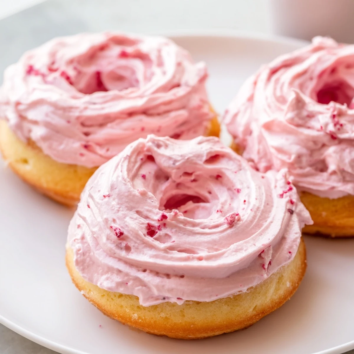Golden Strawberry Buttercream Frosted Donuts piped high with creamy berry frosting and sprinkles