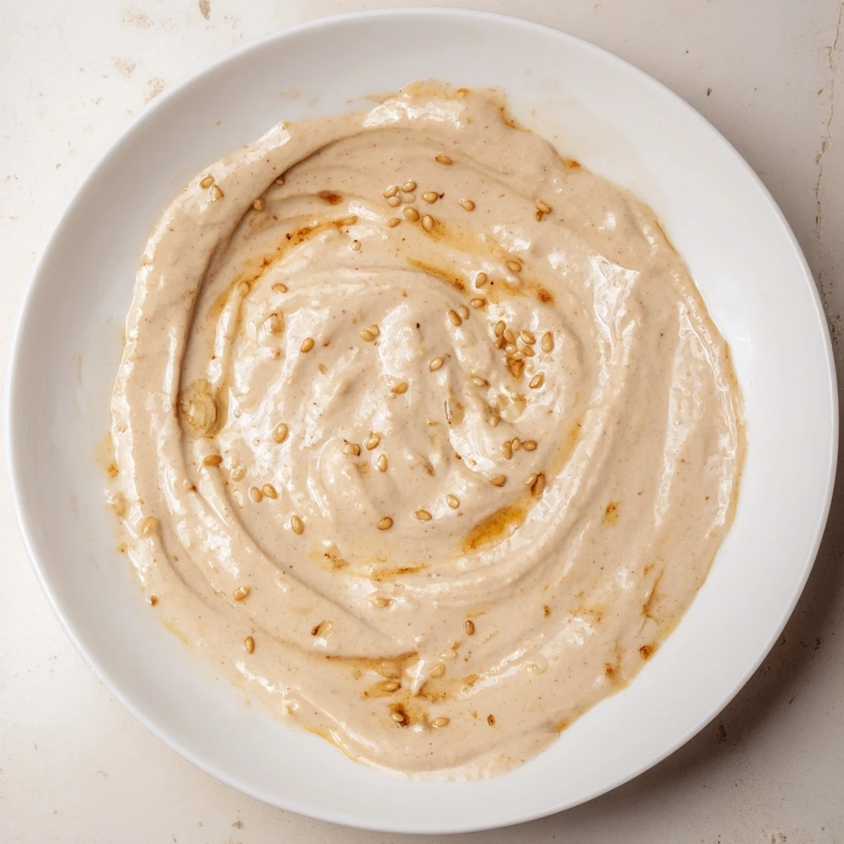 Rich tahini-based sauce with nutty flavor poured beside crisp vegetable grain bowl.
