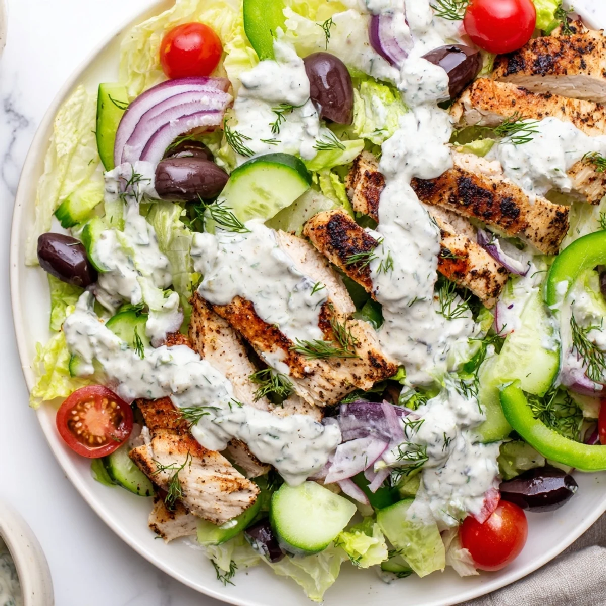 Golden grilled chicken rests on vibrant greens and vegetables in this Greek chicken salad with whipped feta