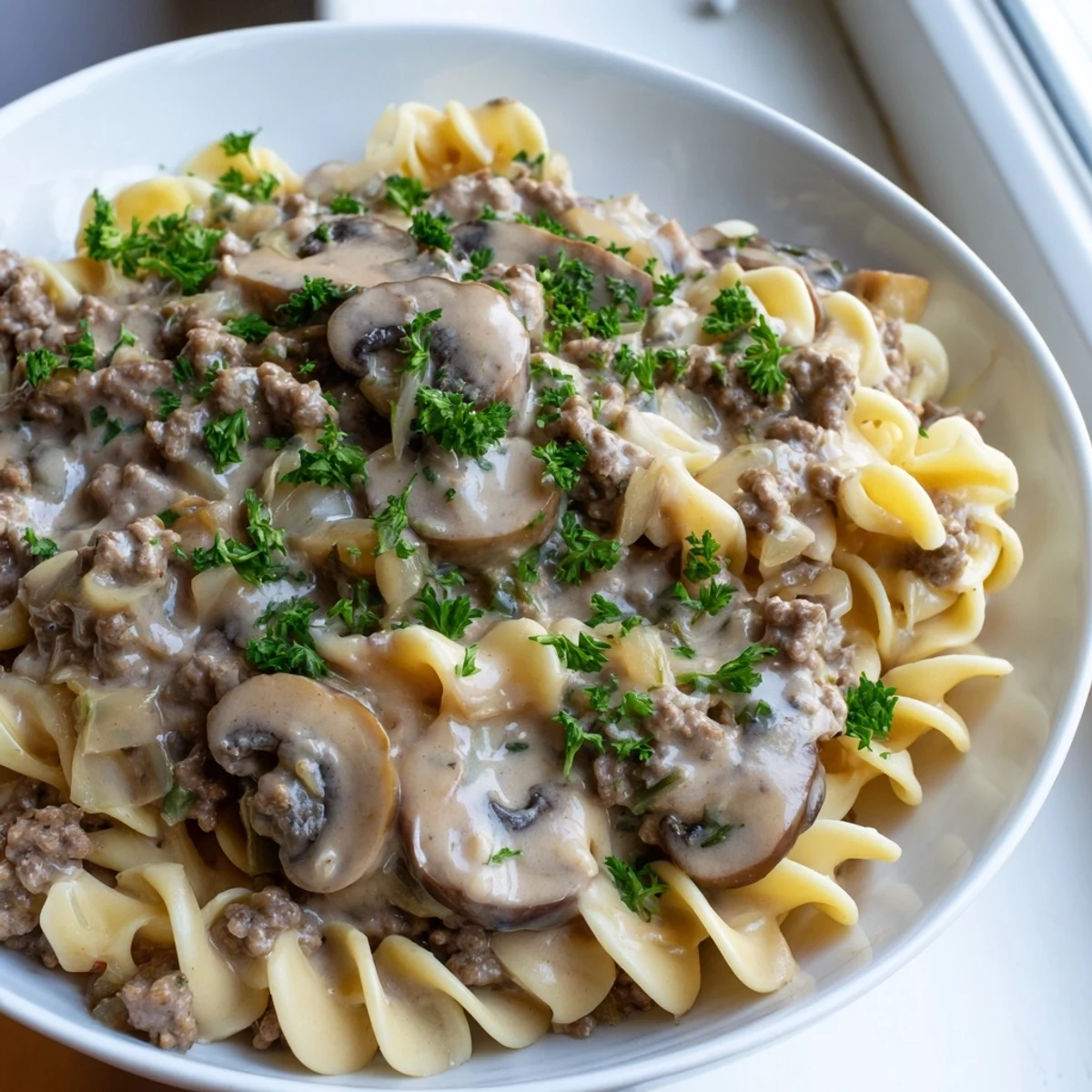 Steaming bowl of hamburger stroganoff with golden egg noodles in rich creamy sauce