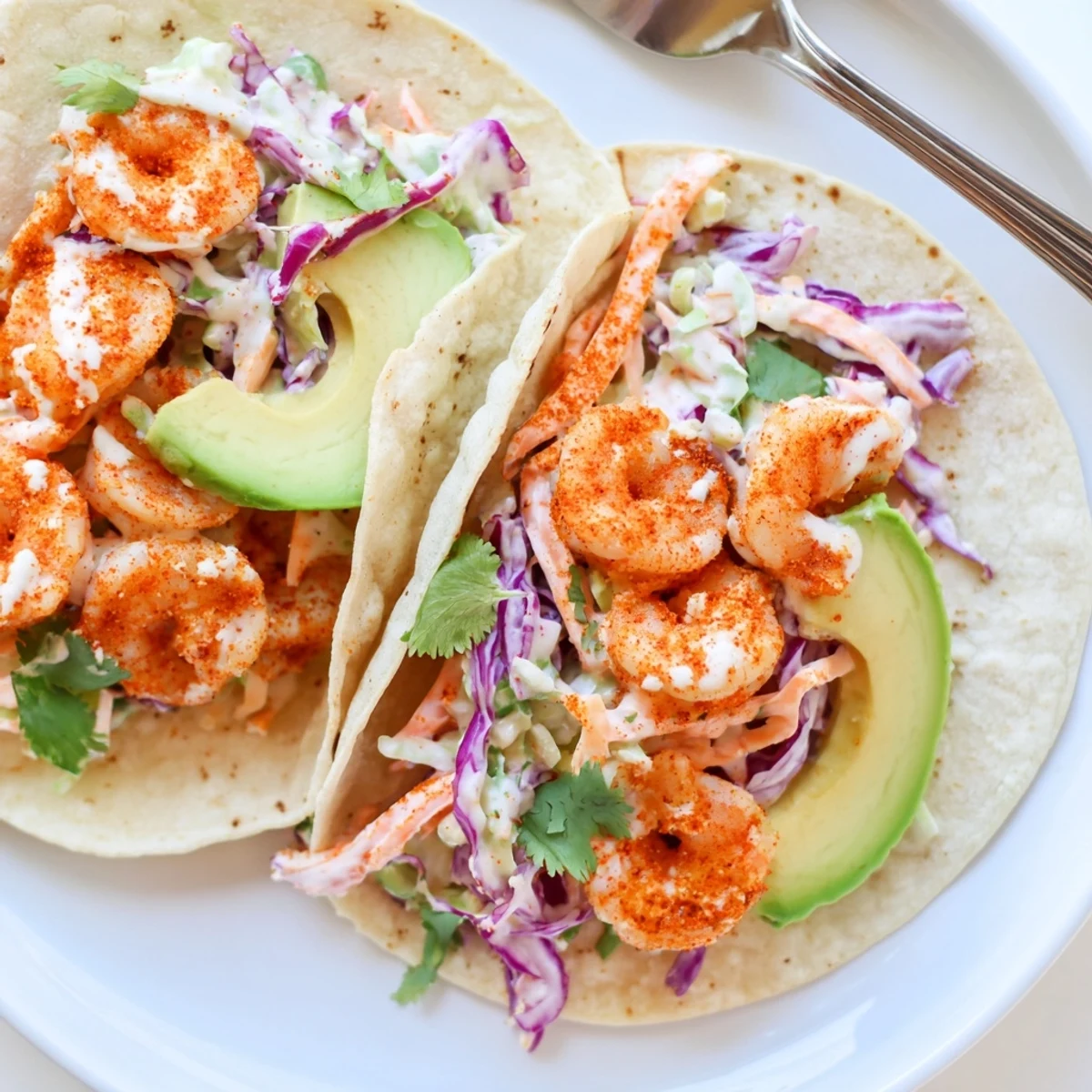 Golden seasoned shrimp nestled in corn tortillas with zesty garlic cilantro lime slaw and cilantro garnish