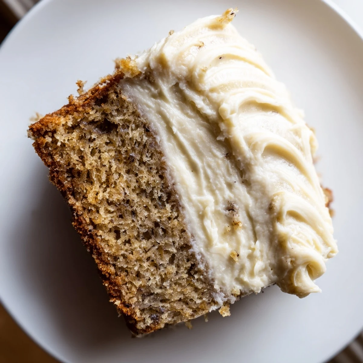 Brown Butter Banana Cake sliced thick with generous cream cheese frosting on a rustic wooden board