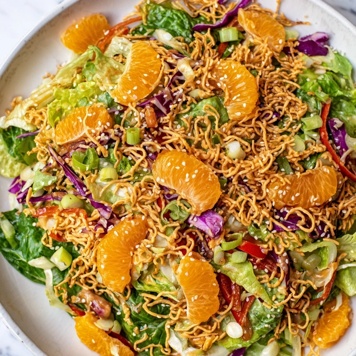 A vibrant Mandarin Sesame Crunch Salad topped with golden noodles and fresh vegetables