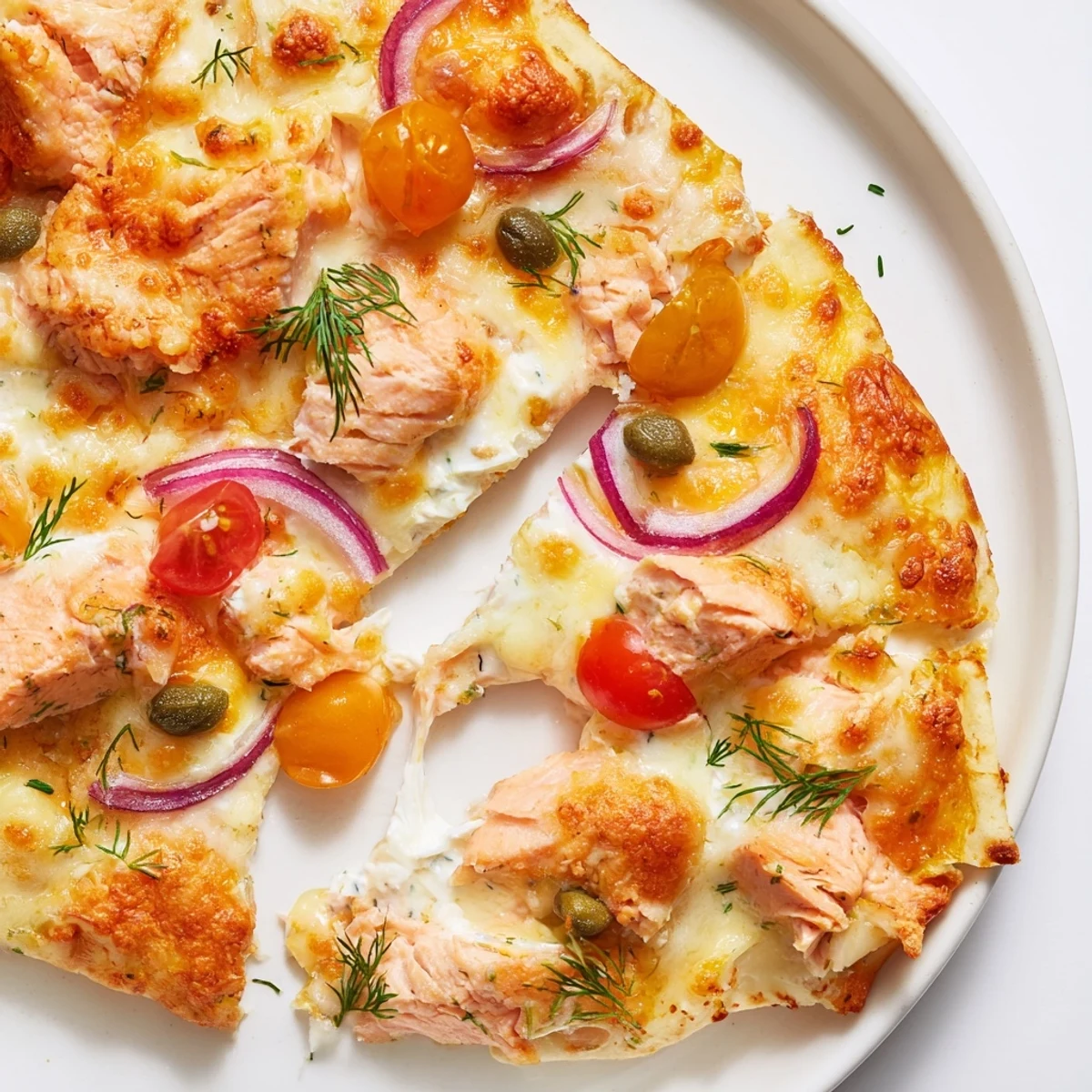 Golden baked salmon tortilla pizza topped with cherry tomatoes, capers, and bubbling cheese.