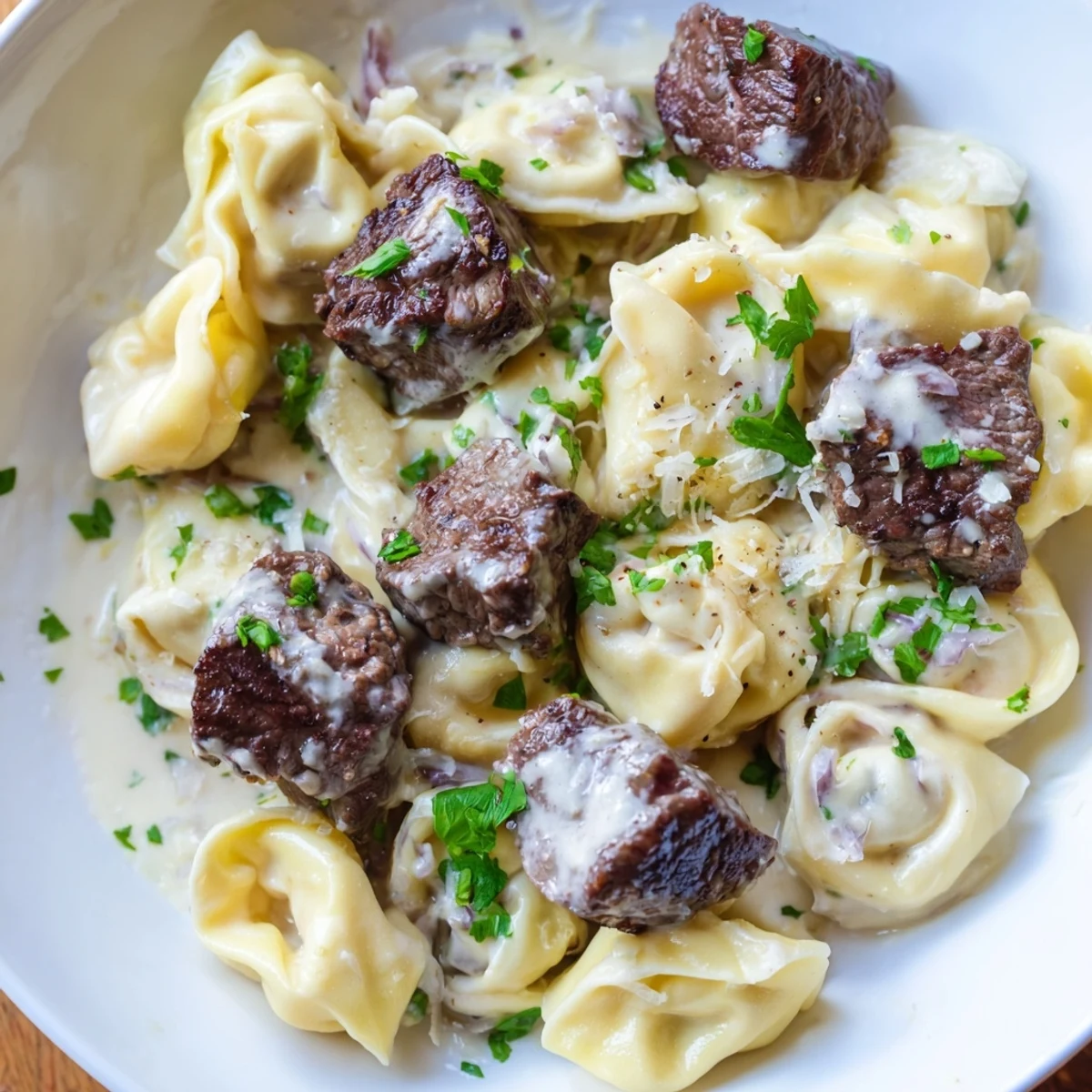 Steaming skillet of Garlic Steak Tortellini garnished with chopped parsley in a rich garlic sauce