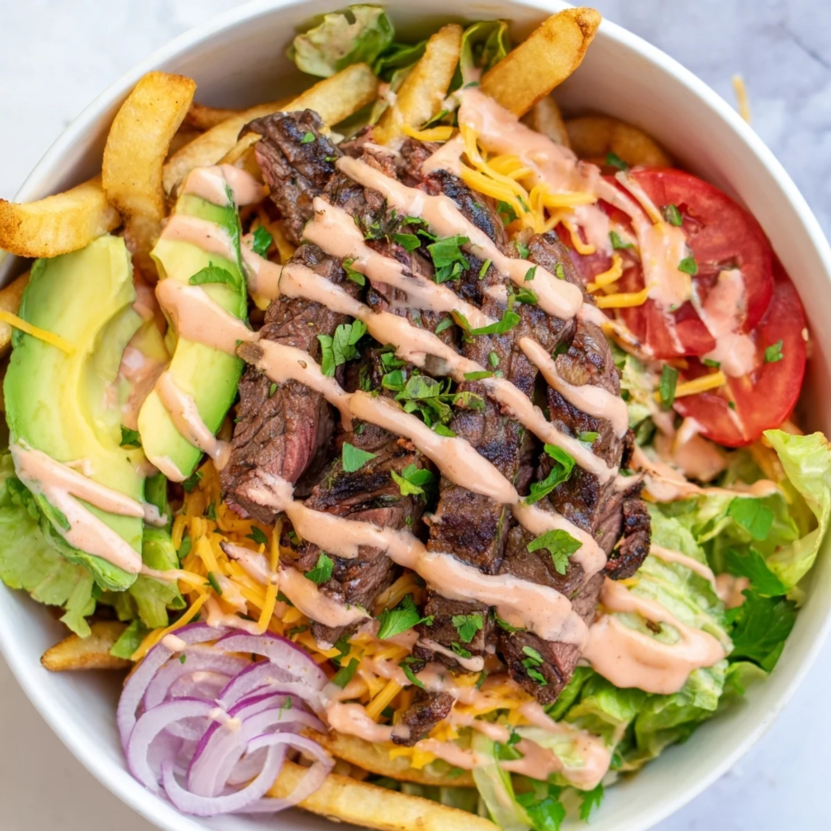 Crispy golden fries topped with seared steak strips and fresh avocado slices in a hearty bowl