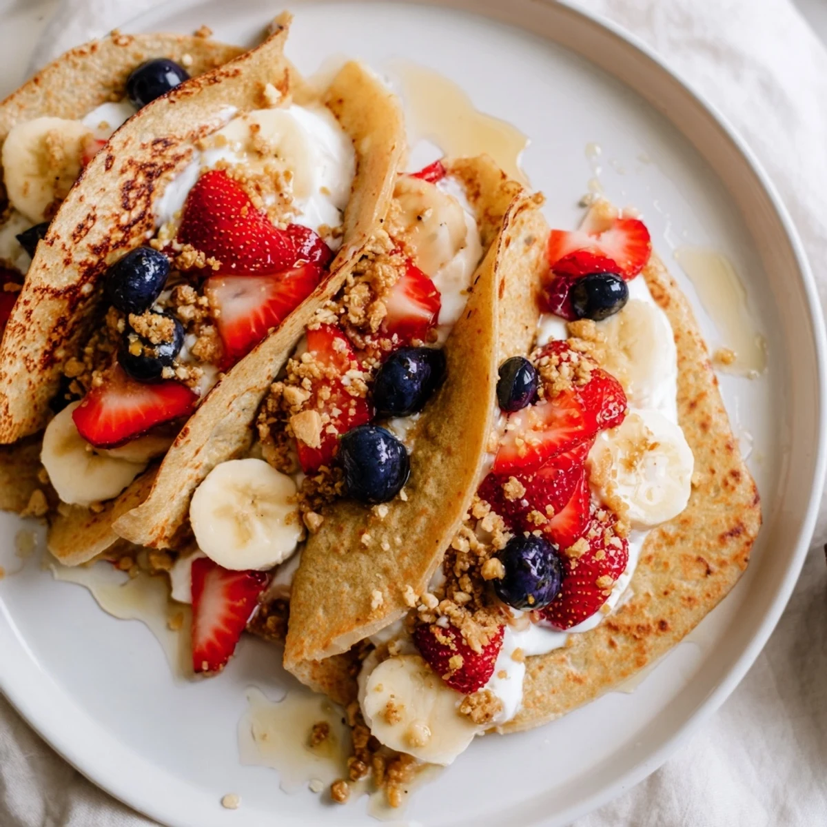 Golden pancake tacos stuffed with fresh berries and drizzled maple syrup on a white plate