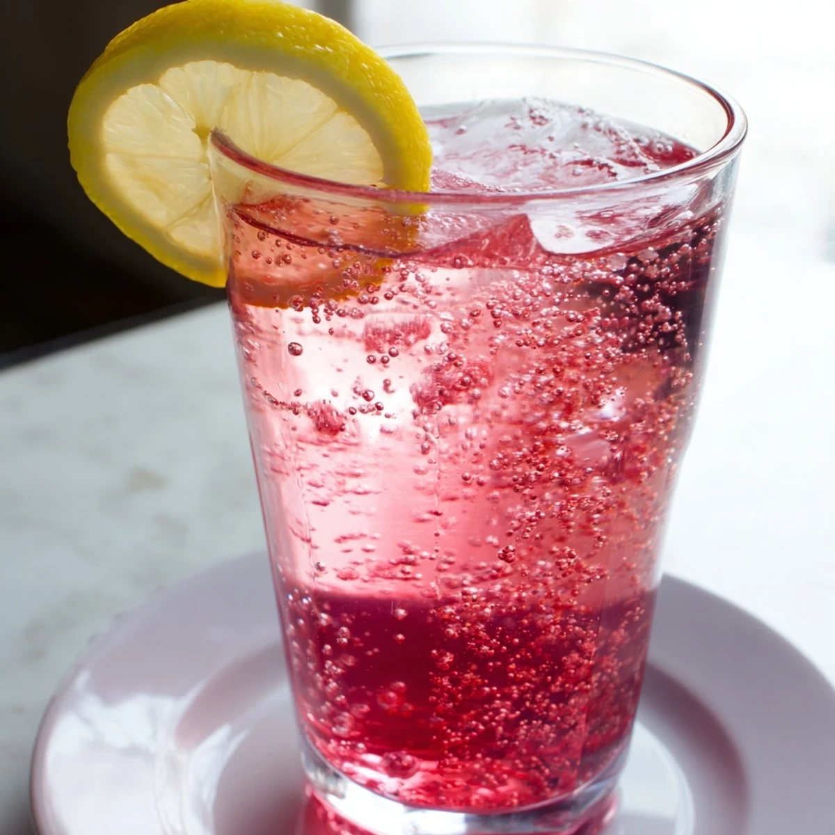 A glass of chilled Refreshing Honey Lemon Pink Soda bubbles with pink cranberry juice.  