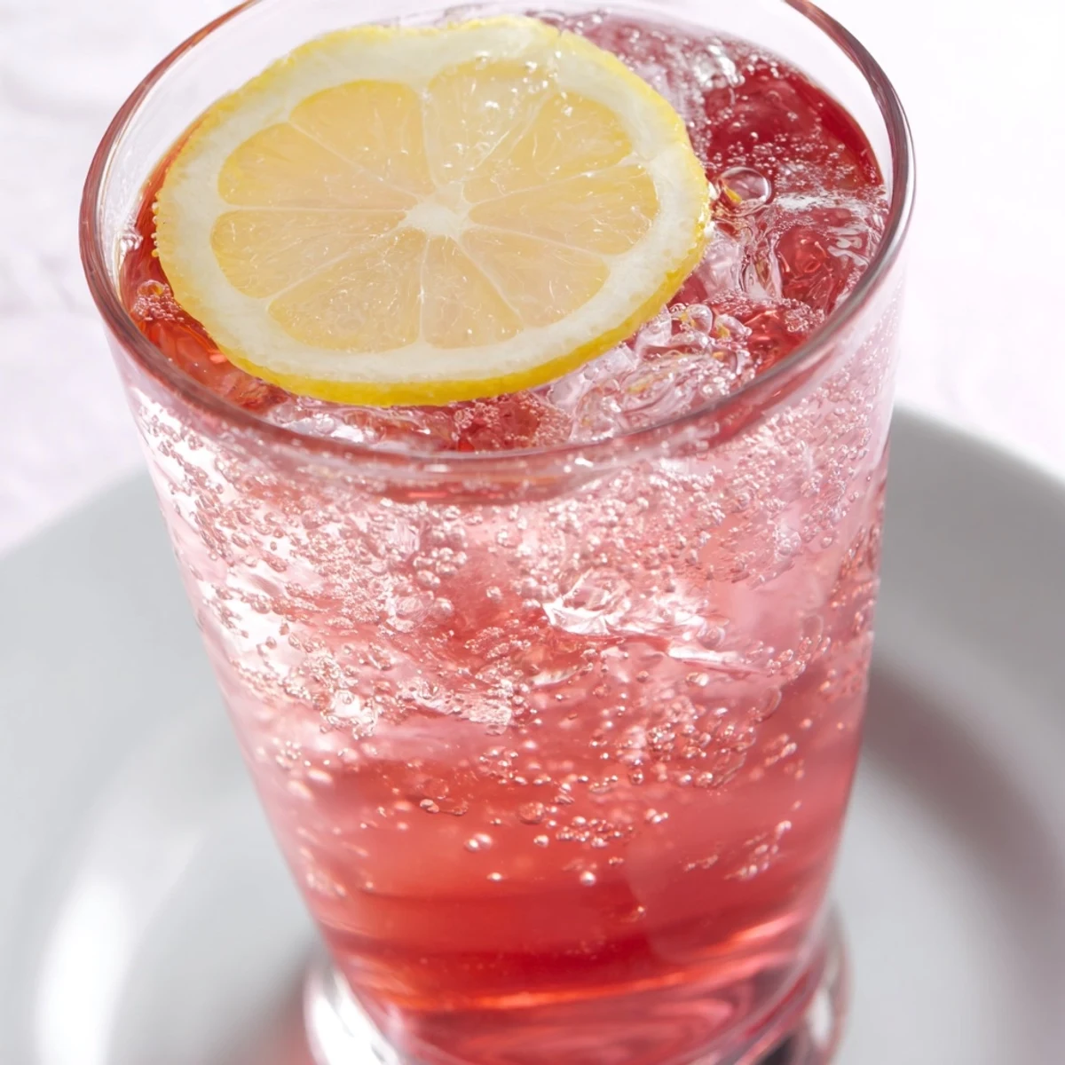 Close-up of Refreshing Honey Lemon Pink Soda garnished with mint and lemon on ice.