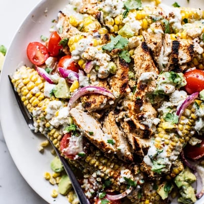 Grilled chicken slices over charred corn and fresh vegetables in a vibrant main dish salad